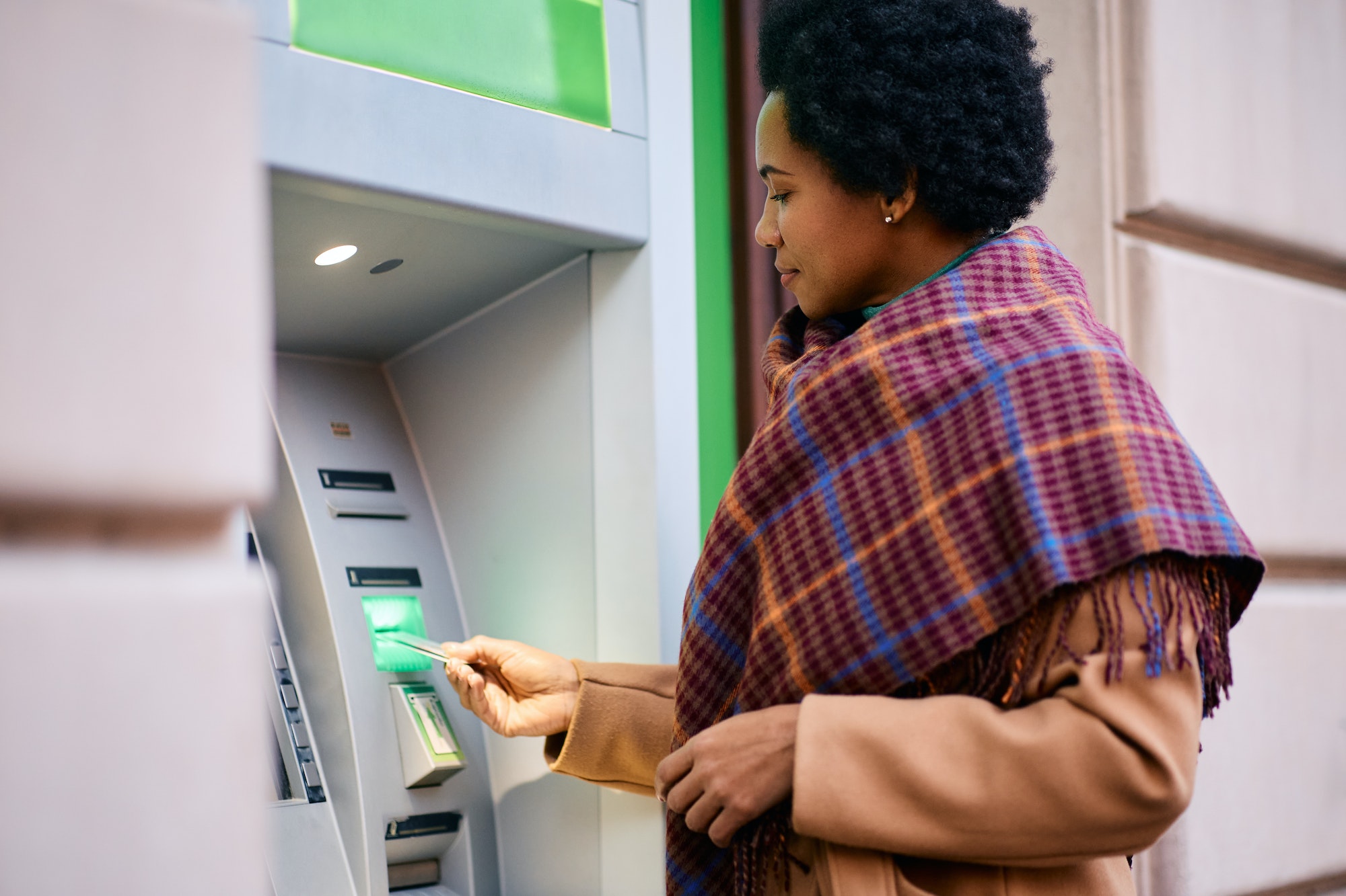 African American woman withdrawing money from ATM machine in the city.