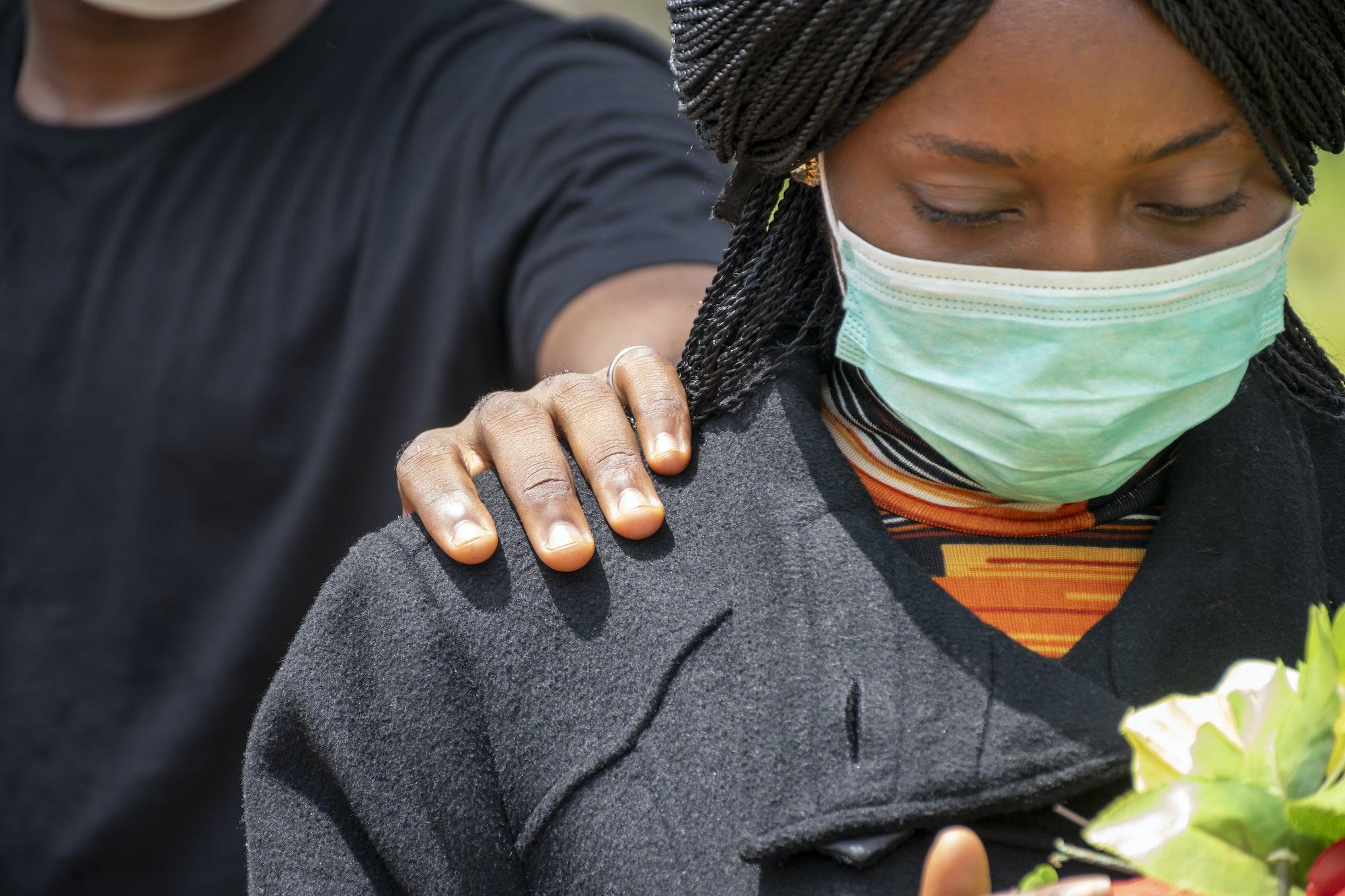 Closeup shot of an African female at a funeral with a hand on her shoulder